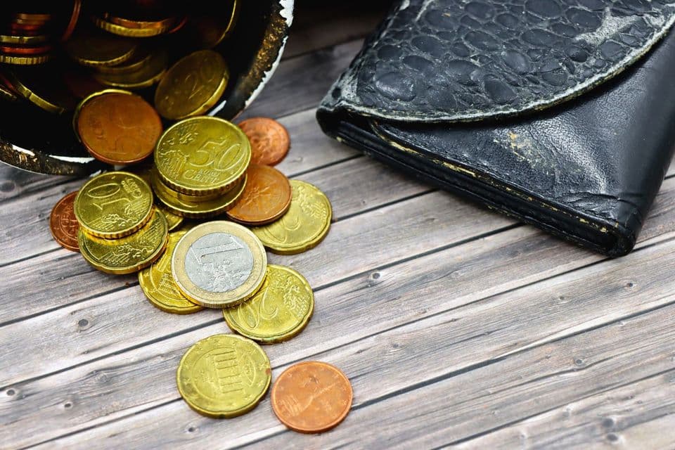 Ošúchaná kožená peňaženka a rozsypané eurové mince na drevenom stole